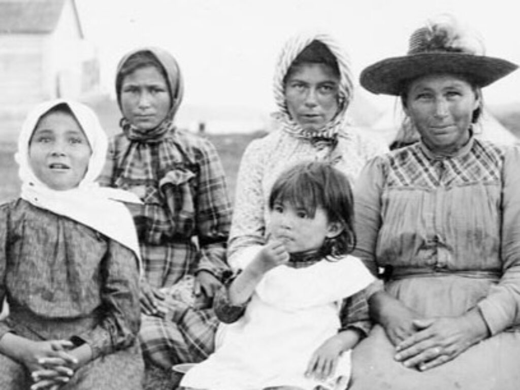 Women and children [of Brunswick House First Nation] at the feast during Treaty 9 payment ceremony at [the Hudson’s Bay Company Post called] New Brunswick House, Ontario.